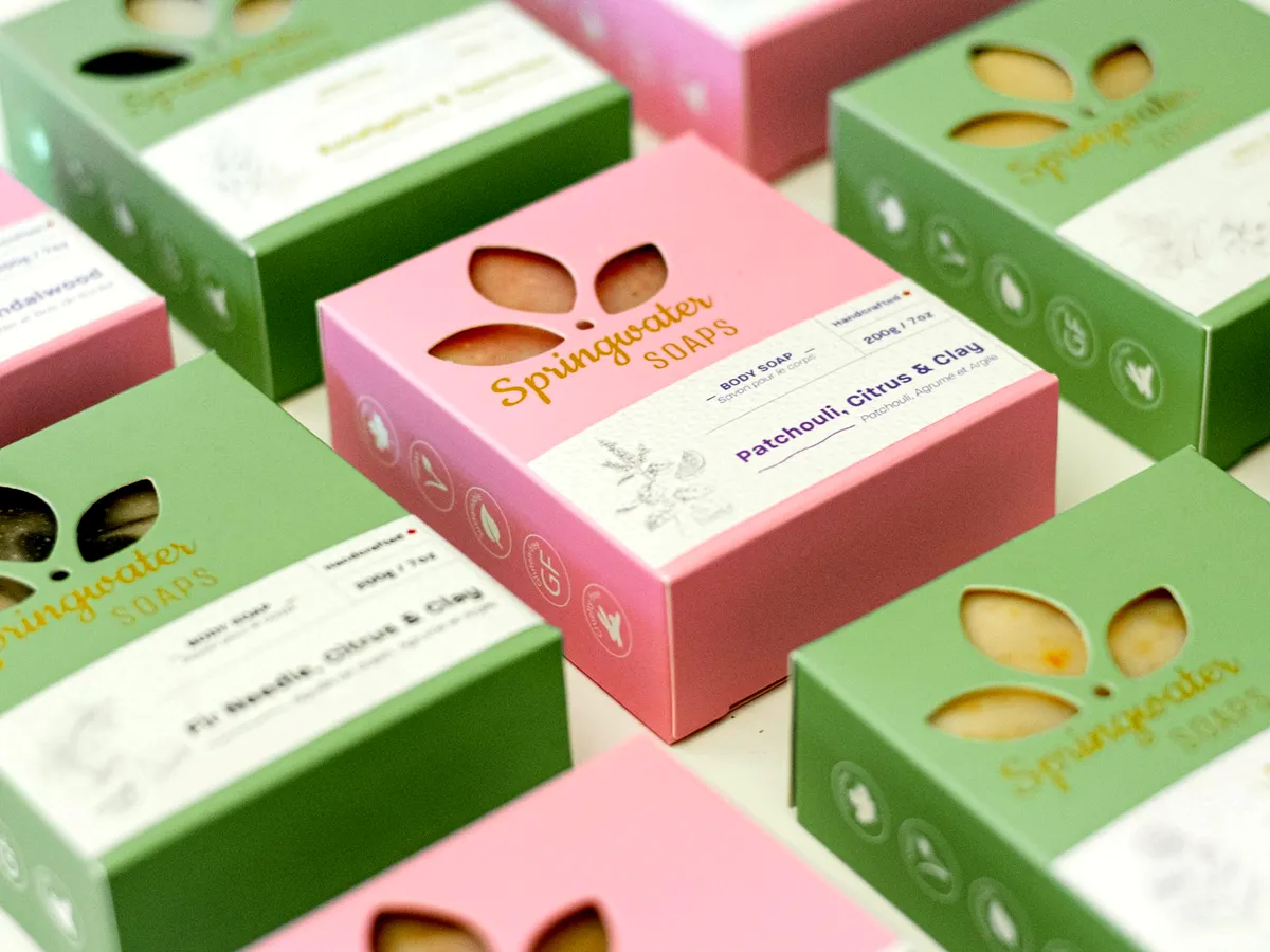 Rows of pink and green soap cartons with die-cut windows and gold foil brand type.