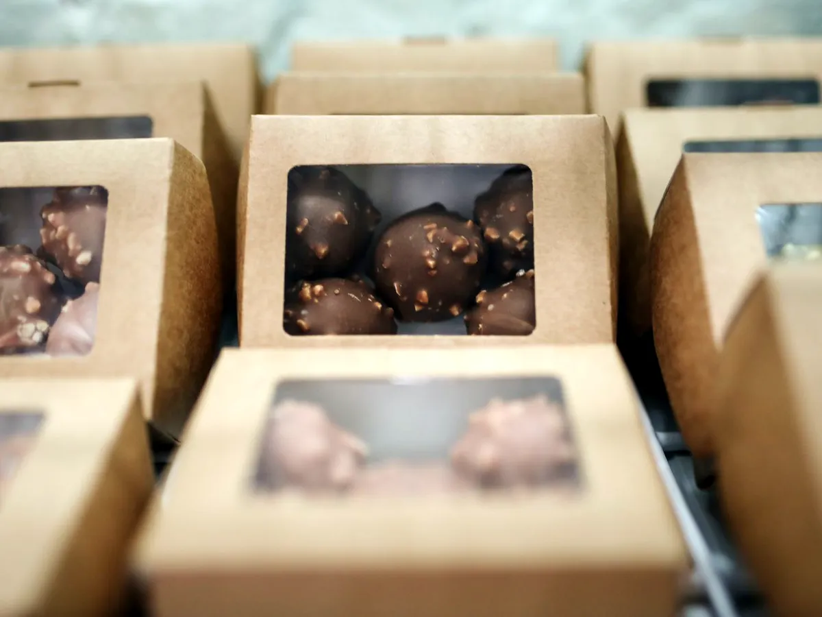 Kraft window-cut display boxes lined up in a counter tray, each holding a chocolate truffle.