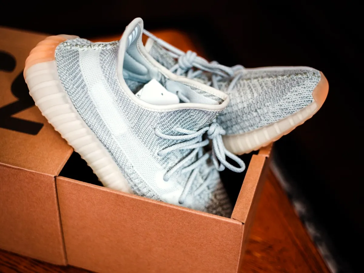 A knit sneaker resting on the open lid of a kraft shoe box on a dark table.